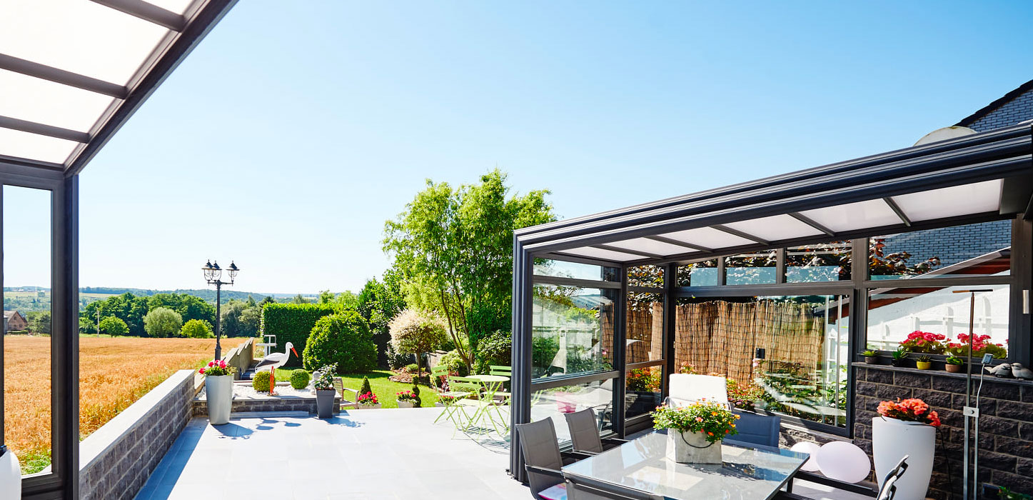 Véranda bioclimatique rétractable installée au-dessus d'une terrasse et du mobilier de jardin qui s'y trouve