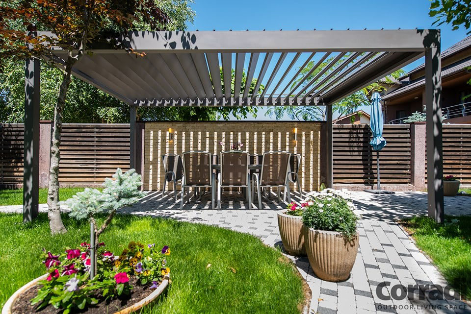 Pergola bioclimatique anthracite dans un jardin très fleuri et arboré