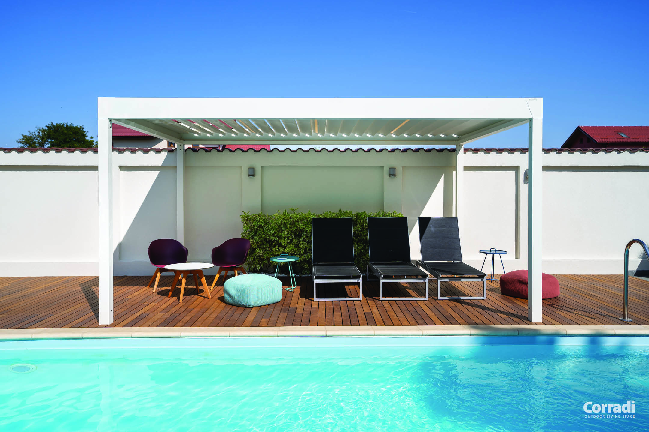 Pergola bioclimatique blanche Corradi aménagée avec des transats et des chaises à ras de la piscine