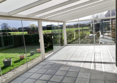 vue de l'intérieur d'une grand véranda toute vitrée de couleur blanche sur une terrasse en carrelages