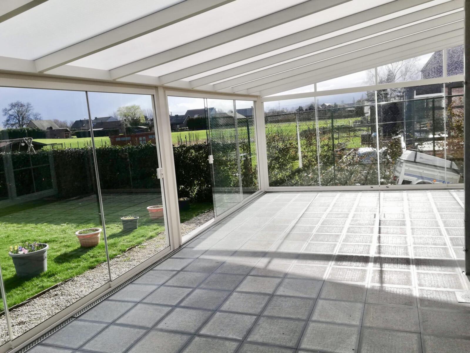 vue de l'intérieur d'une grand véranda toute vitrée de couleur blanche sur une terrasse en carrelages