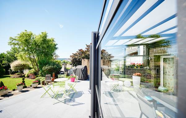 Baie vitrée qui ferme une pergola et donne une vue sur le jardin et les plantes vertes