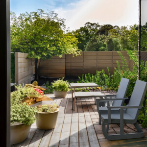 Terrasse extérieure avec des chaises longues blanches et des plantes en pots, entourée d'un jardin verdoyant et de clôtures en bois, offrant un espace de détente et de relaxation en plein air.