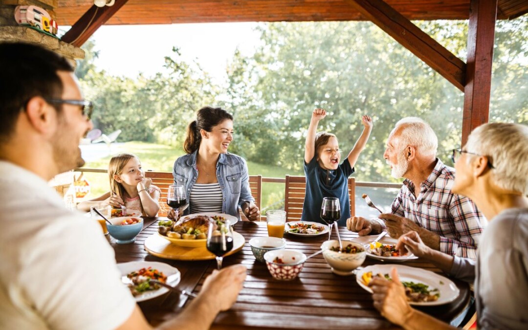 Une famille composée d'enfants, de leurs parents et de leurs grands-parents prend un repas sur la terrasse extérieur protégée par une protection de terrasse