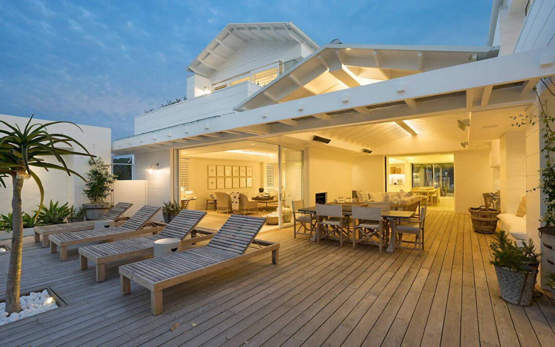 Patio blanc pour aménager la terrasse extérieur en bois, composée de transats en bois, d'une table à manger et d'un palmier.