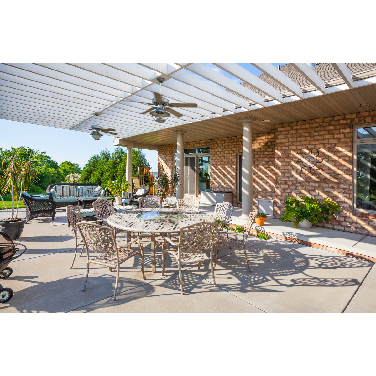 Pergola blanche recouvre une grande terrasse aménagée avec un salon extérieur en tissu et une table avec des chaises