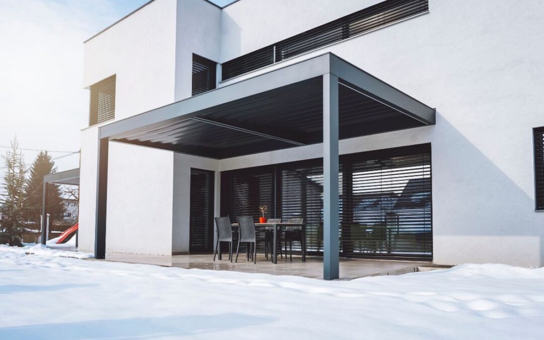 Pergola moderne accolée à une maison blanche. Il y a de la neige