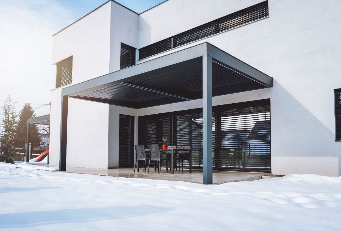 Pergola moderne accolée à une maison blanche. Il y a de la neige