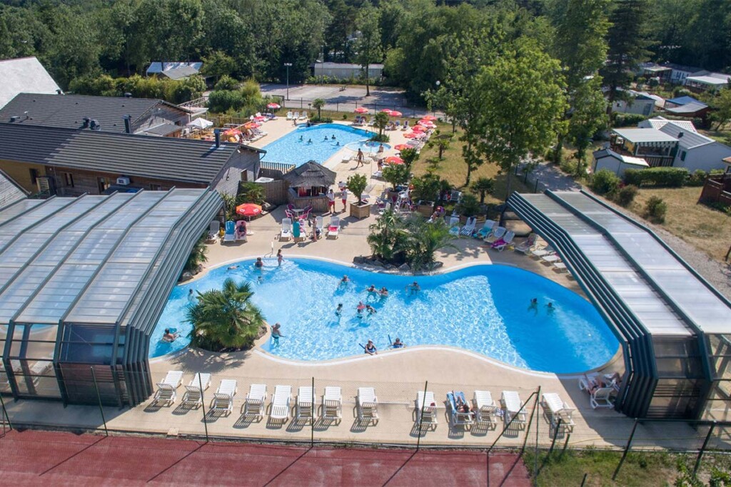 Abri de piscine haut amovible pour collectivité. Il y a plusieurs piscines, des transats, des personnes qui s'amusent