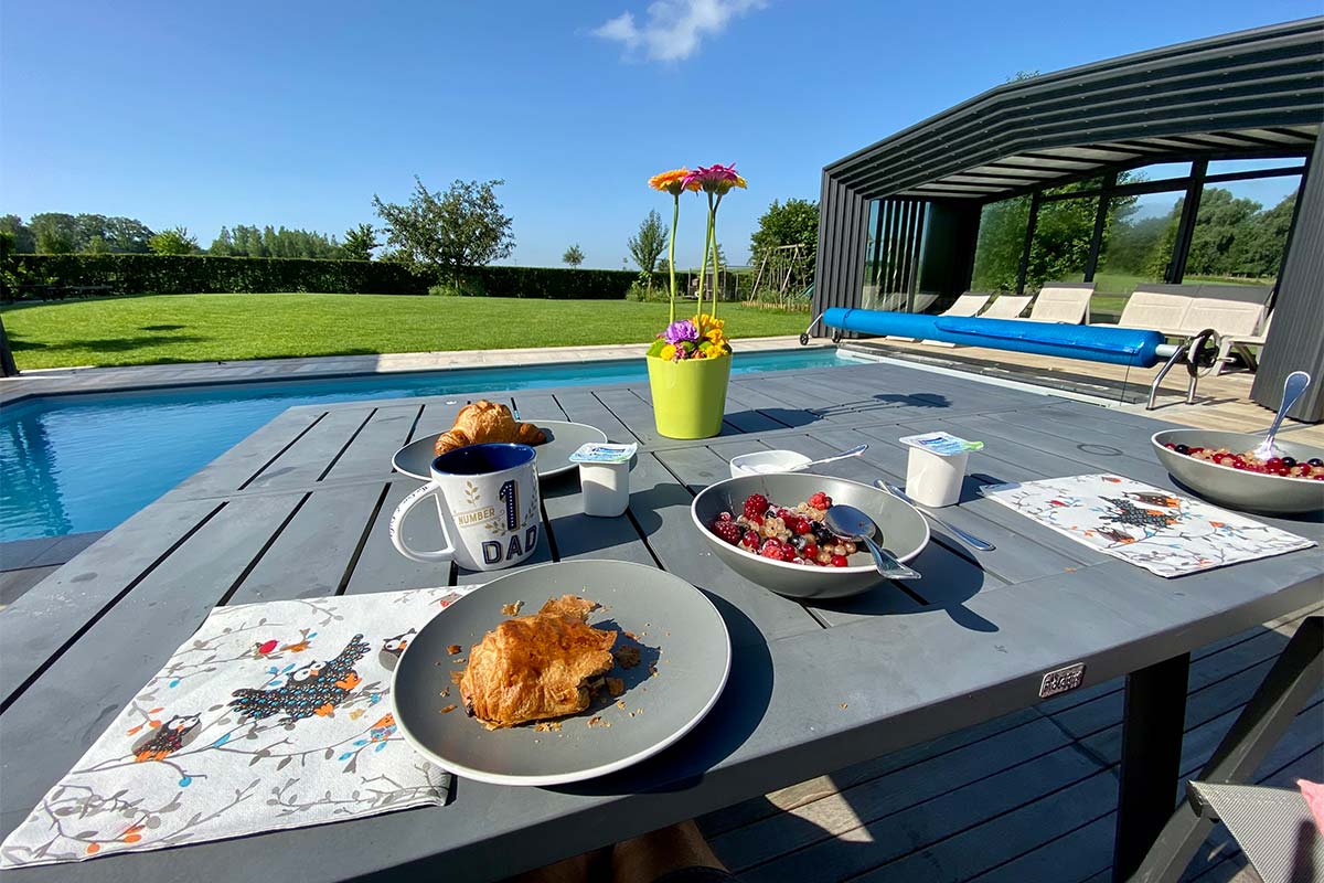 Table avec petit déjeuné et vue sur la piscine et abri de piscine haut amovible