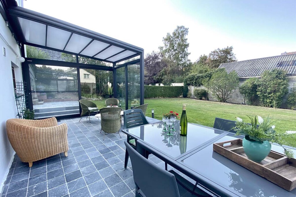 Abri de terrasse rétractable avec vue sur le jardin, chaises , tables et bouteille de vin