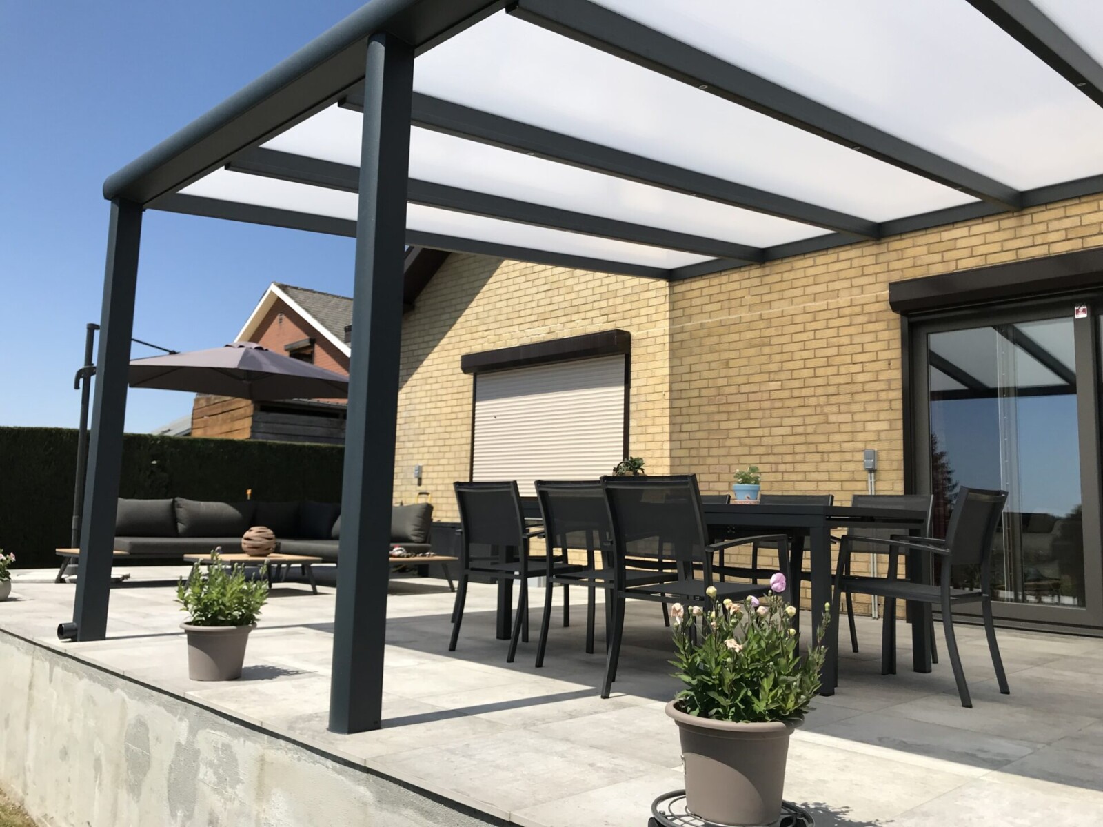 Pergola toit fixe ouverte sur une terrasse avec une table, des chaises et un fauteuil