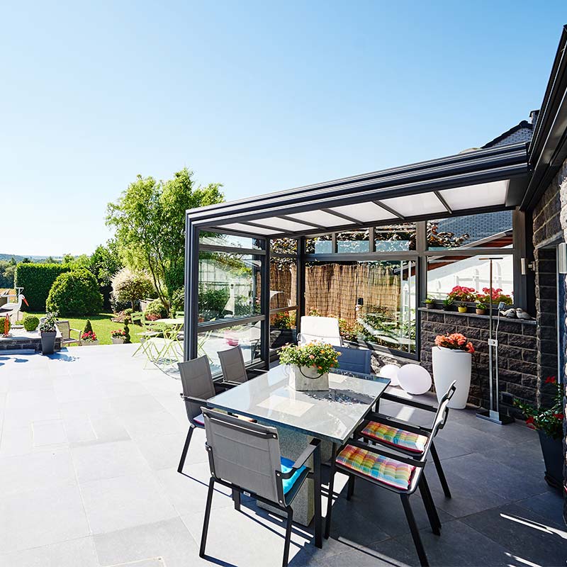 Abri de terrasse rétractable ouvert avec grande terrasse, vue sur le jardin, table et chaises