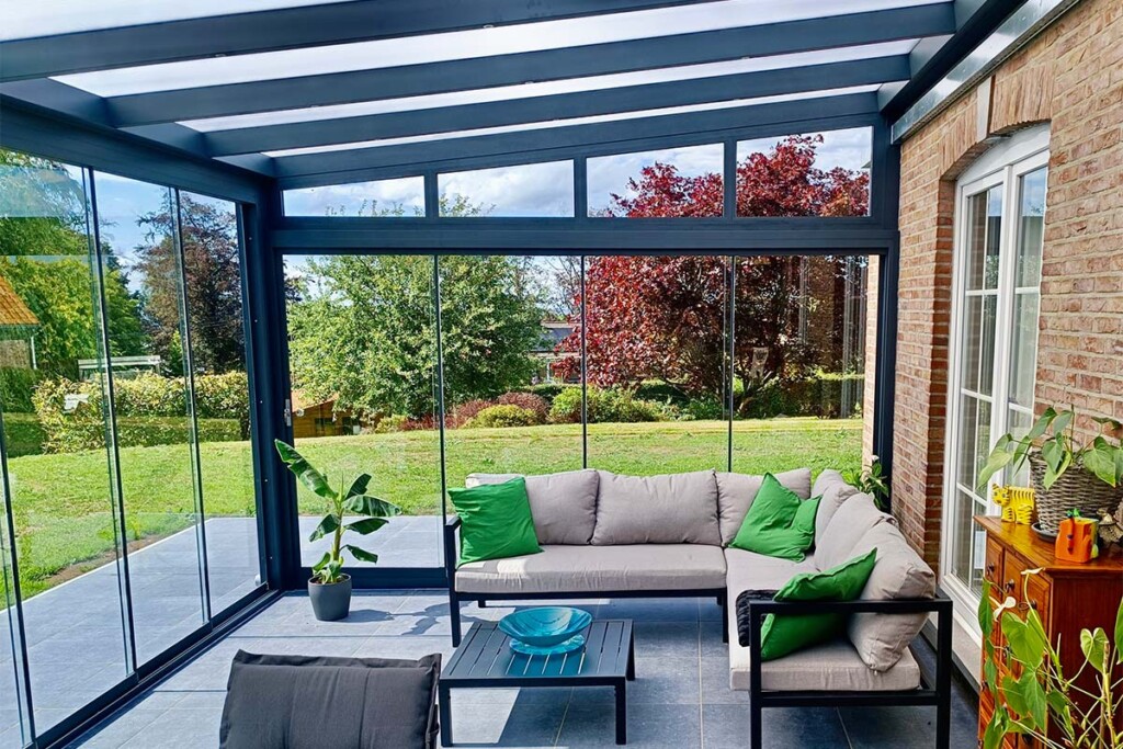 Pergola vitrée avec vue sur le jardin et fauteuil gris