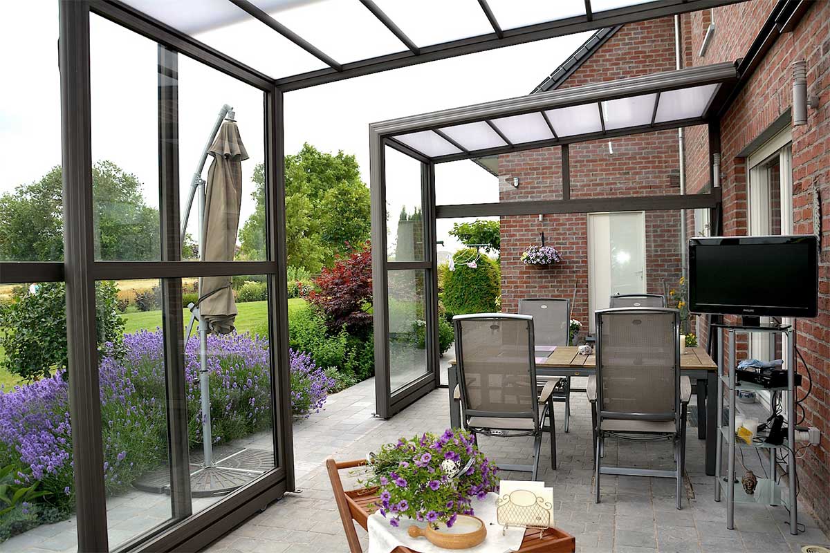 Abri de terrasse rétractable avec table, chaises, tv et vue sur un jardin fleuri