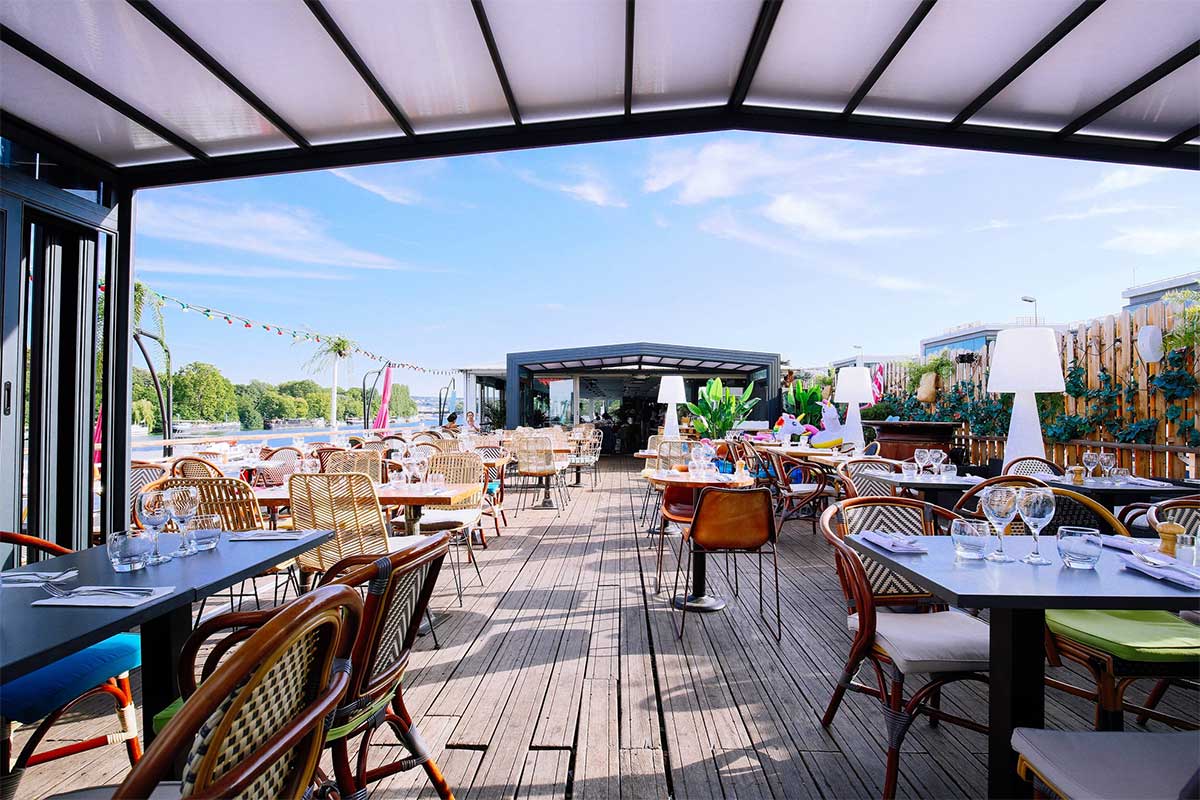 Abri de terrasse ouvert sur une terrasse en bois avec des chaises et des tables dressées