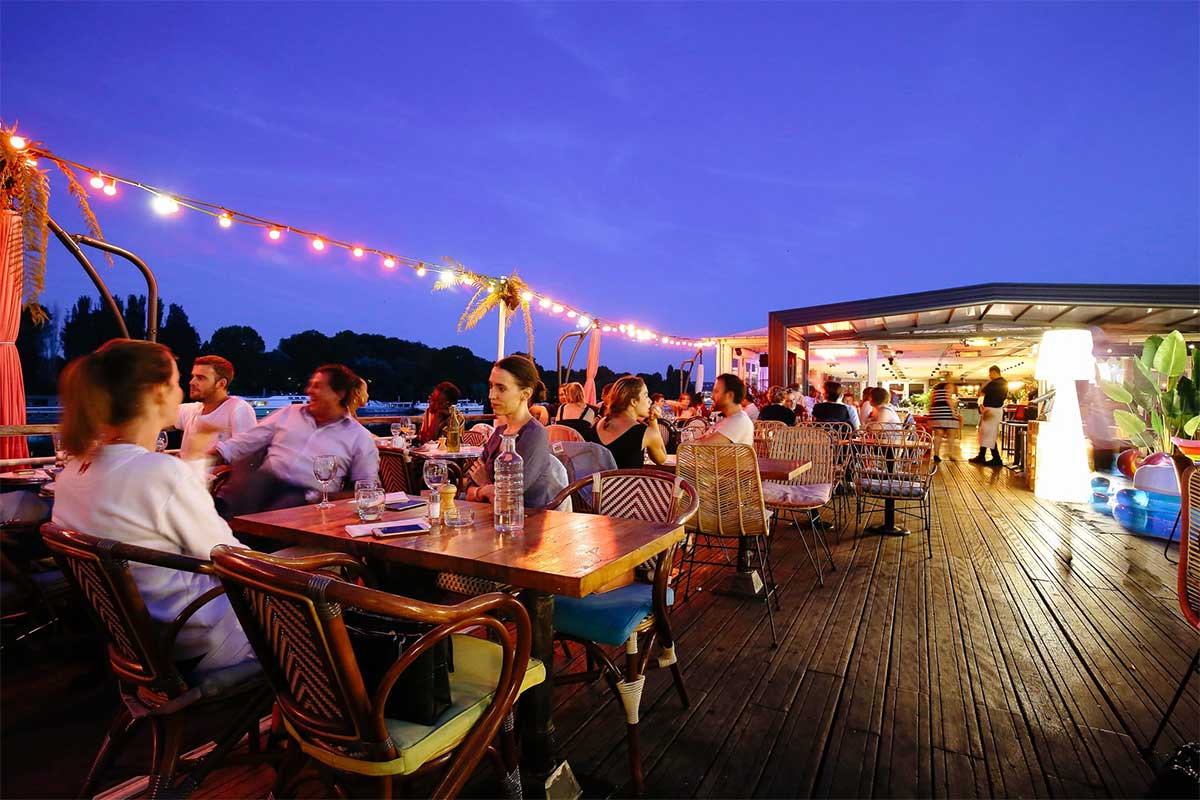 Abri de terrasse restaurant le soir, illuminé avec des guirlandes. Il y a des gens heureux assis aux tables