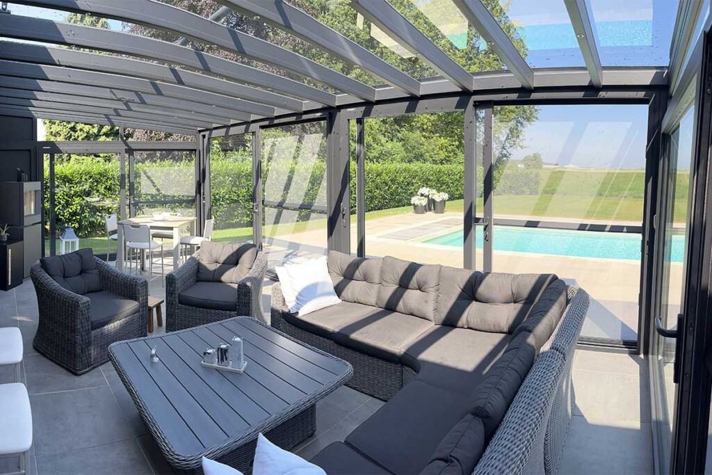 Pergola vitrée avec fauteuils, table et avec vue sur une piscine