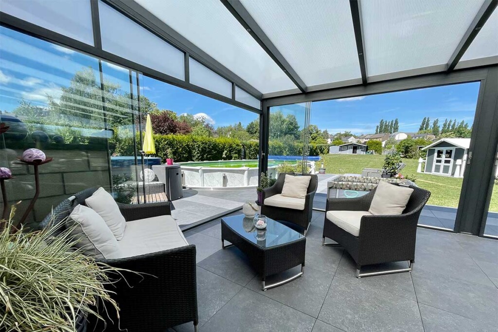 Pergola vitrée avec fauteuil et vue sur le jardin avec une piscines et des abris de jardin