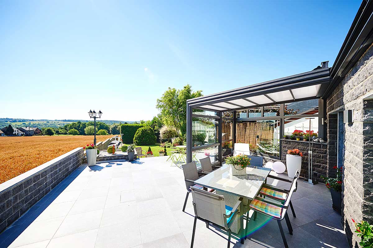 Abri de terrasse rétractable sur une grande terrasse avec une table, des chaises, des fleurs et avec une vue sur le jardin et un champ