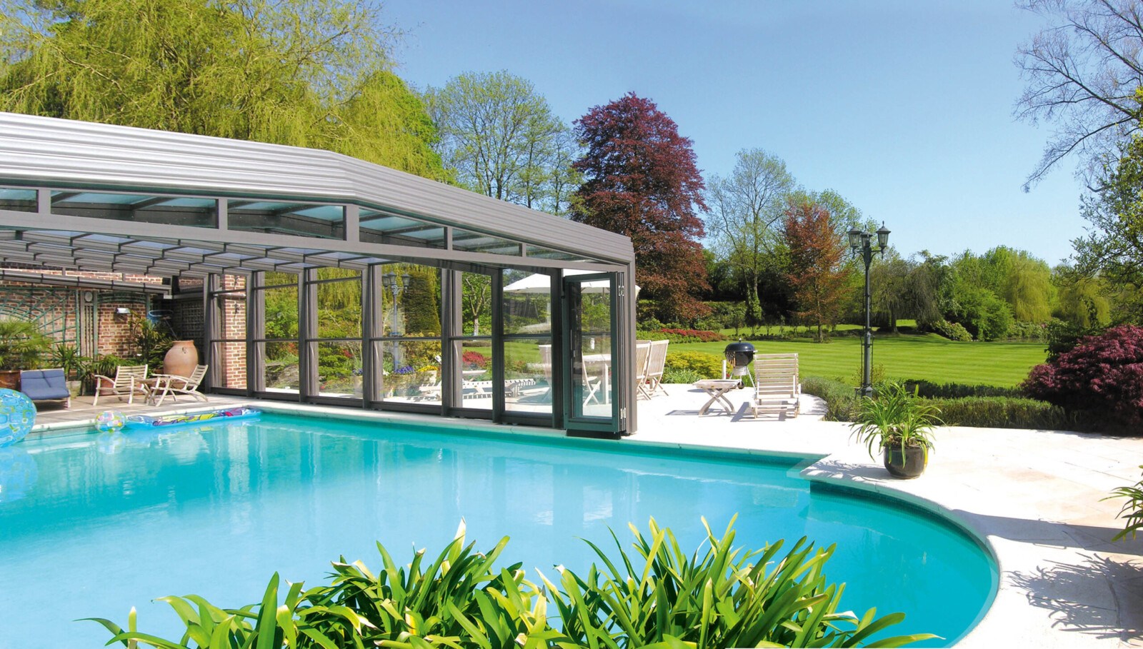 Abri de piscine haut amovible dans un grand jardin avec des transats, un barbecue, des chaises, une table et une grande pelouse