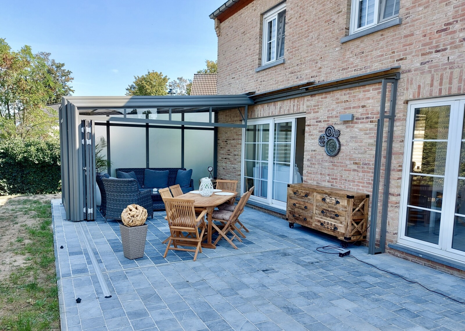 Maison en briques rouges claires avec une terrasse en pierres bleues et un abri de terrasse adossé au mur