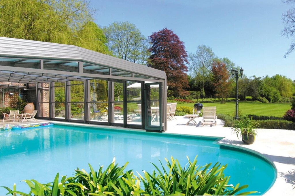 Abri de piscine haut et amovible situé dans un vaste jardin équipé de transats, d'un barbecue, de chaises, d'une table et d'une grande pelouse.