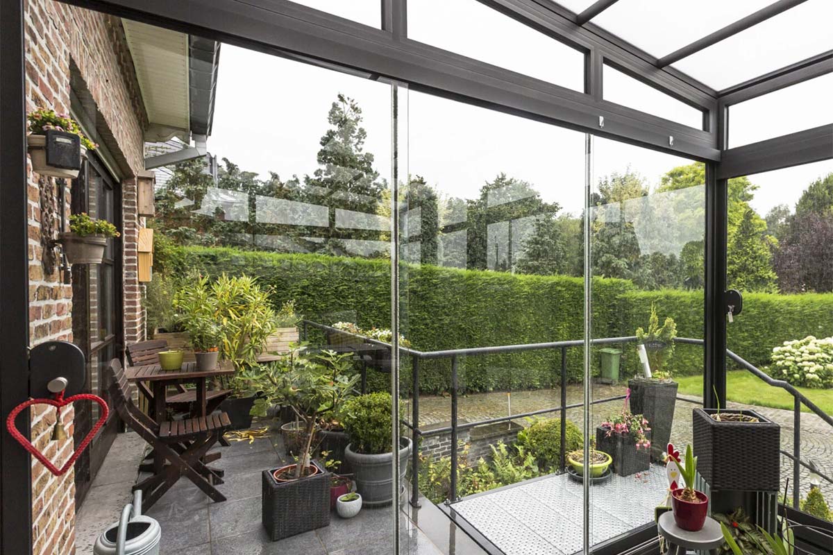 Pergola vitrée avec une baie vitrée coulissante avec vue sur le jardin et le reste de la terrasse