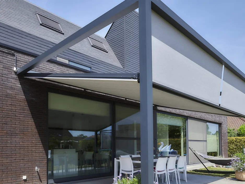 Véranda rétractable sur une terrasse carrelée à ras du jardin, composée d'une table en verre et des chaises en osier