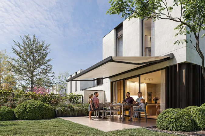 Véranda rétractable sur une terrasse carrelée à ras du jardin, composée d'une table en verre et des chaises en osier