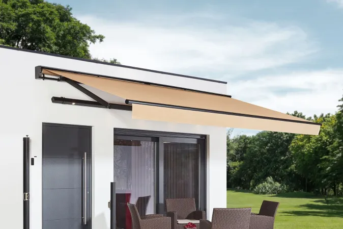 Véranda rétractable sur une terrasse carrelée à ras du jardin, composée d'une table en verre et des chaises en osier